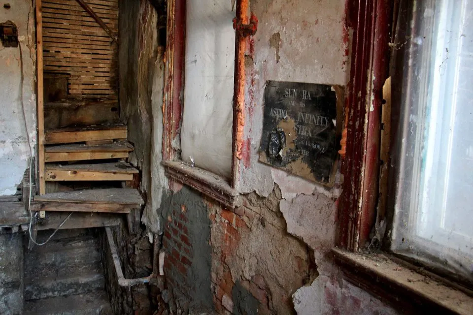 partially collapsed interior of old house with torn and faded vintage Sun Ra concert poster on crumbling wall