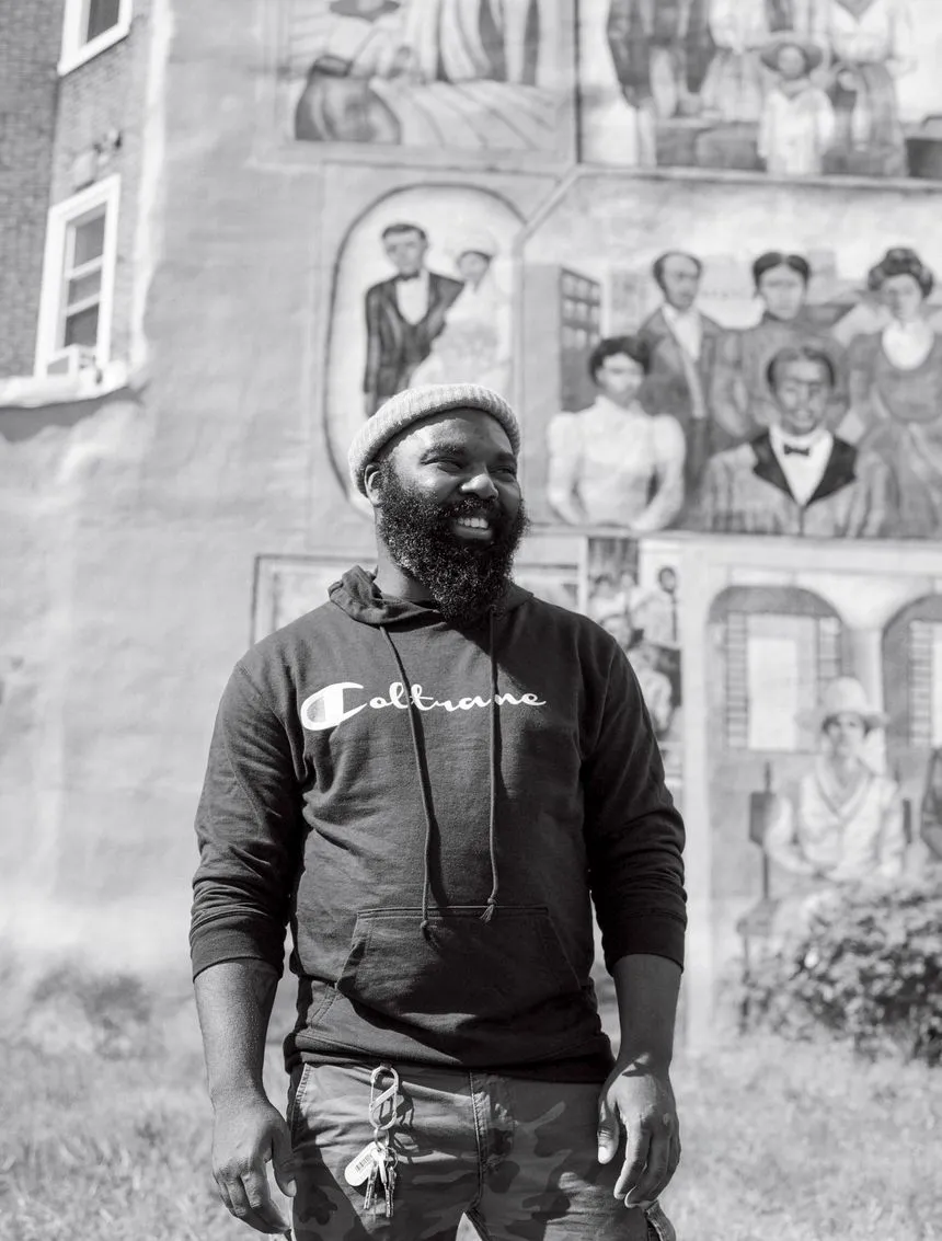 Omar Tate stands in front of a mural in the Mantua neighborhood of Philadelphia.